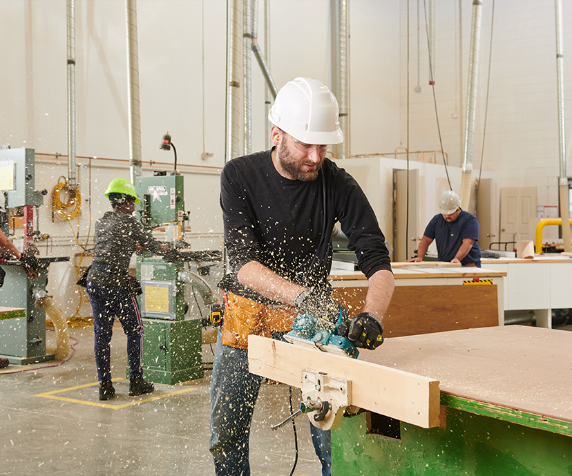 Carpentry student using a skill saw along a piece of wood that is clamped to a workstation.
