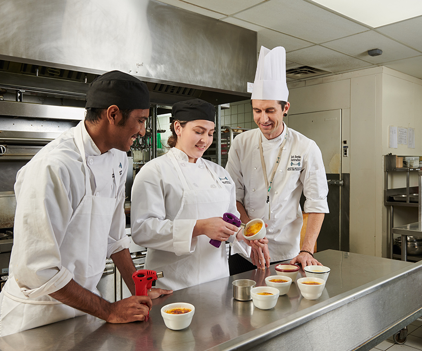 Two students working with their teacher making creme brulee