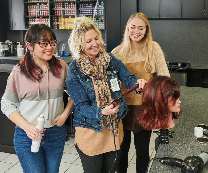 Two students and instructor practicing cutting hair on a mannequin.