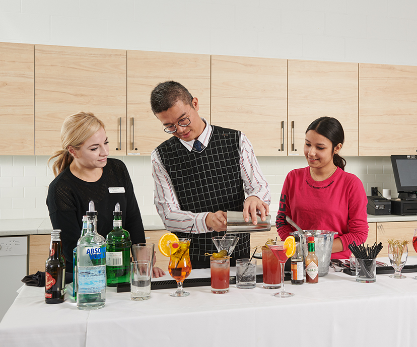 Three student standing at a serving table, making mocktails.
