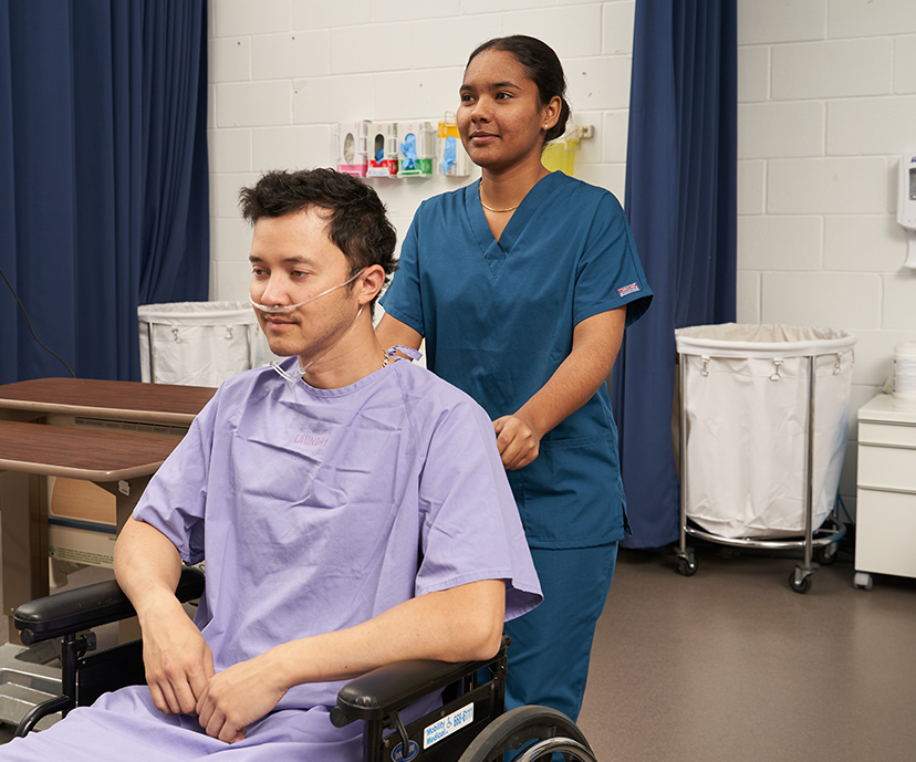 Two students, one sitting in a chair wearing a respirator, the other standing behind him, check his vitals